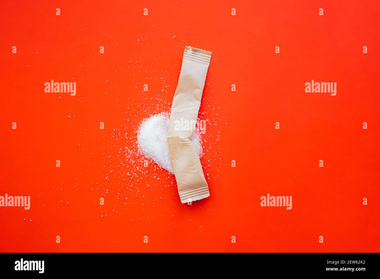 Bâton de papier cassé avec du sucre renversé sur fond rouge vif. Photographie abstraite de produit, sucre et consommation de sucre doux, espace de copie Banque D'Images