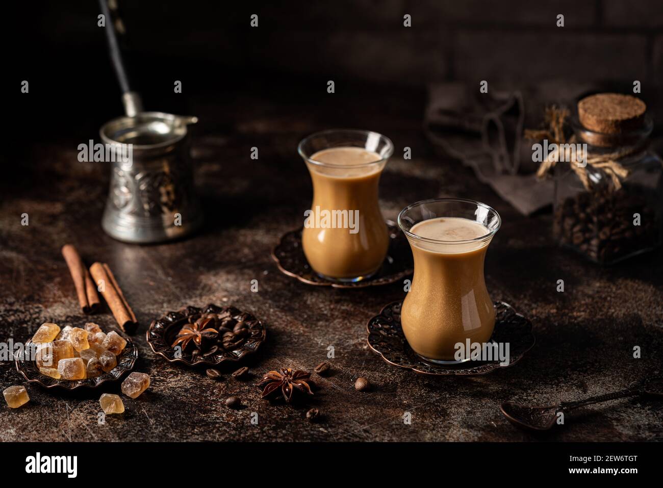 Thé ou café avec lait et épices en verre Armudu avec grains de café et sucre sur fond sombre. Banque D'Images