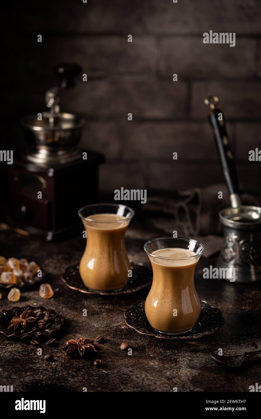 Thé ou café avec lait et épices en verre Armudu avec grains de café et sucre sur fond sombre. Banque D'Images