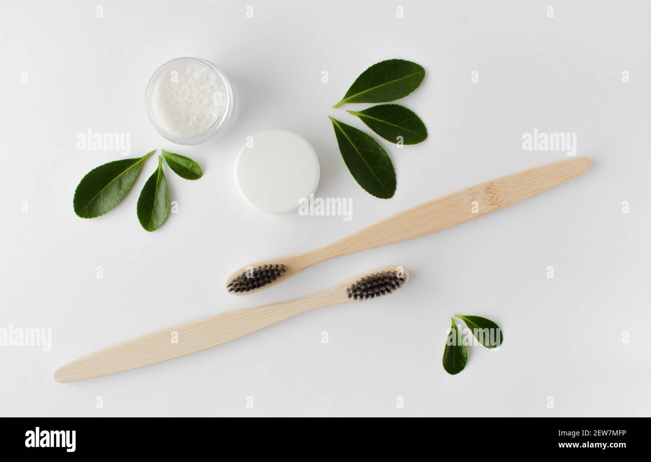 deux brosses à dents écologiques en bambou en bois, dentifrice et feuilles vertes sur fond blanc. Banque D'Images