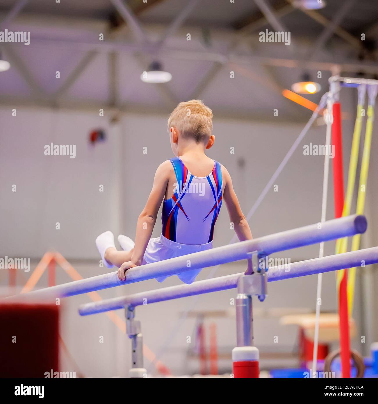 Un petit garçon en vêtements de sport effectue un exercice sur les barreaux inégaux. Gymnastique rythmique, entraînement dans le hall. Banque D'Images