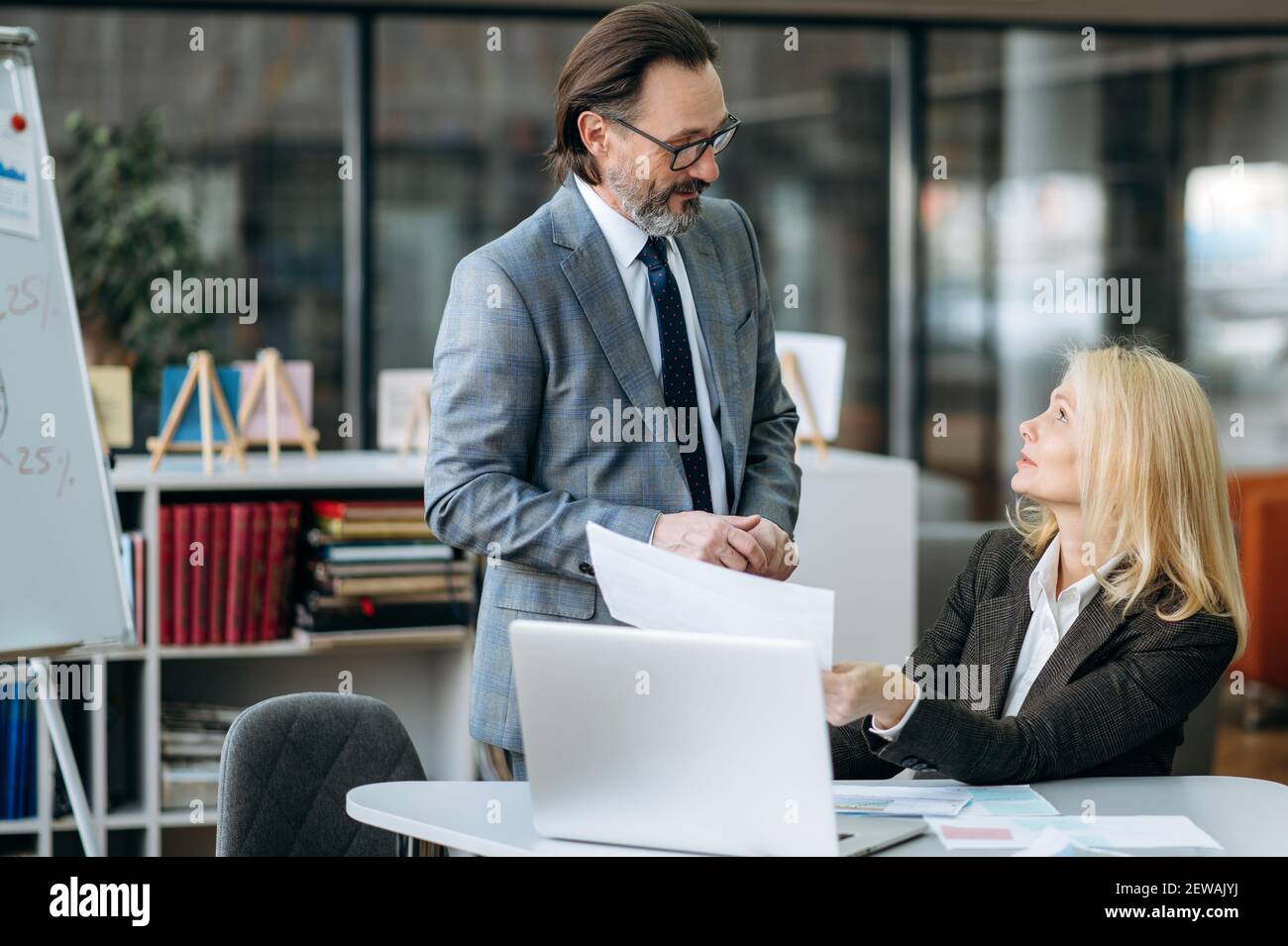 Des collègues sérieux d'âge moyen travaillant sur un projet d'entreprise, discutant d'un nouveau plan. Élégante femme blonde-cheveux demander des conseils sur les graphiques financiers de collègue de sexe masculin Banque D'Images