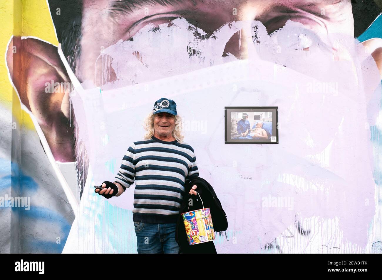 Milan, Italie. 26 février 2021. Un homme âgé qui pose à proximité d'un portrait annulé portant un masque facial.des portraits dédiés aux travailleurs de la santé de l'hôpital Luigi Sacco et aux proches des victimes de Covid-19, ont été représentés par l'artiste Cosimo Cheone, Et les associations locales, avec la coopération de la municipalité locale, en juillet 2020, dans le quartier de Quarto Oggiaro à Milan. Les peintures murales ont été récemment détruites en novembre 2020 par des inconnus, offensant la mémoire de ceux qui avaient combattu Covid-19. Crédit: Valeria Ferraro/SOPA Images/ZUMA Wire/Alay Live News Banque D'Images