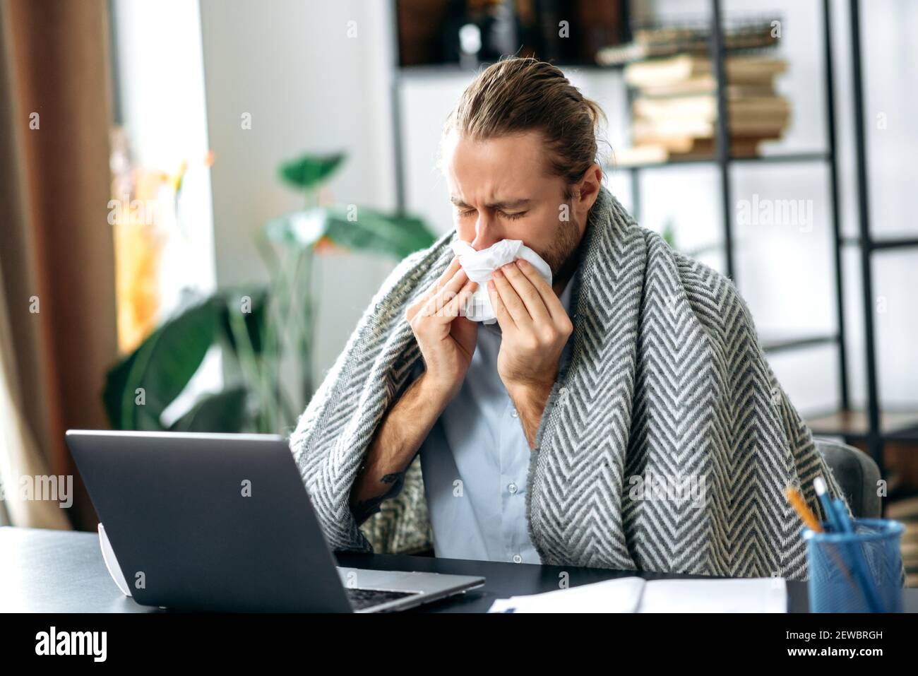 Homme caucasien s'assoir au bureau, travaillant à distance ou étudiant, tandis que la maladie, en utilisant le papier de soie, éternuant. Insain homme freelance malaise, malade avec le nez courant Banque D'Images