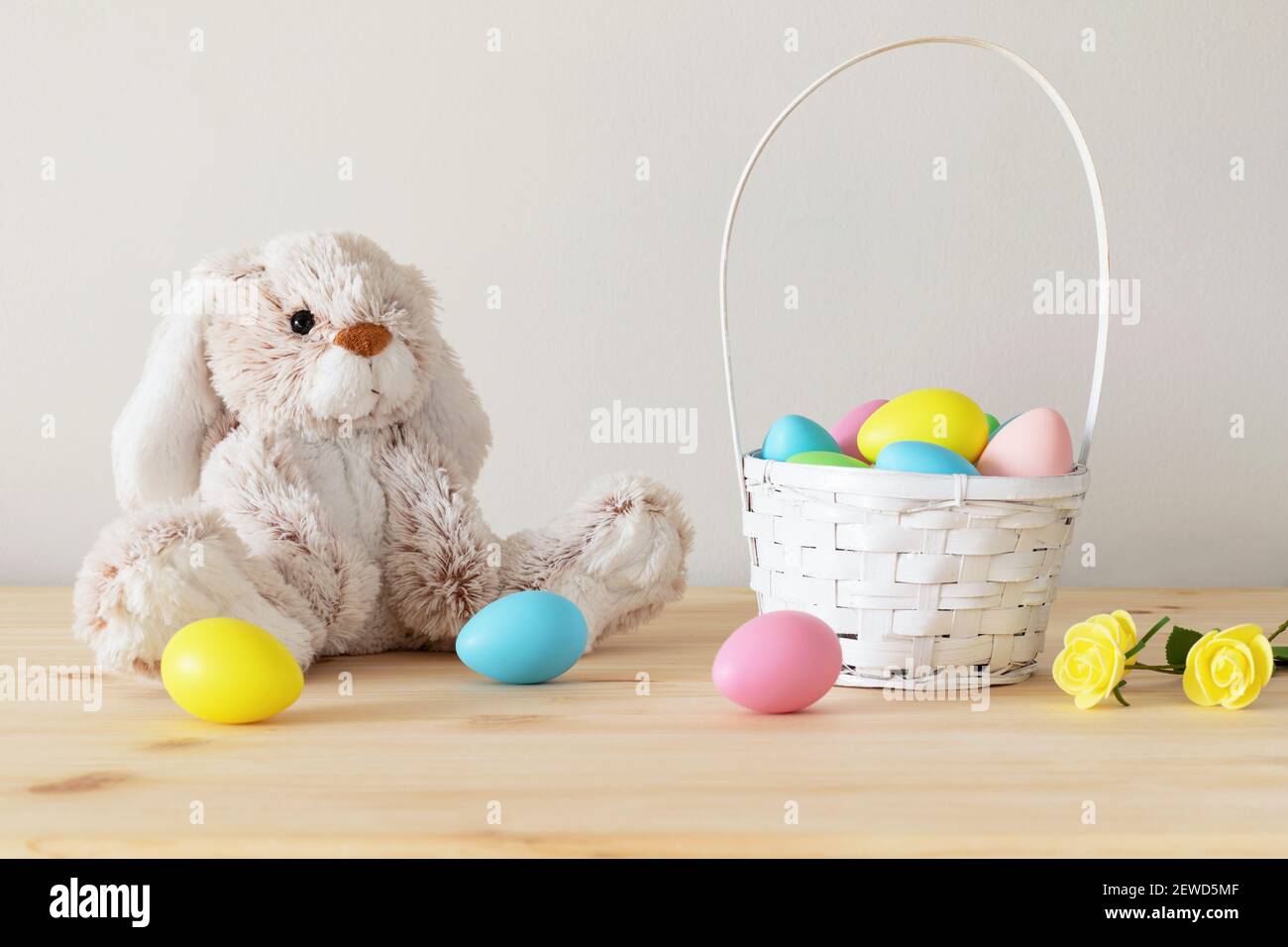Lapin jouet de Pâques, œufs colorés avec panier et petites fleurs sur table en bois avec fond blanc et espace de copie. Banque D'Images