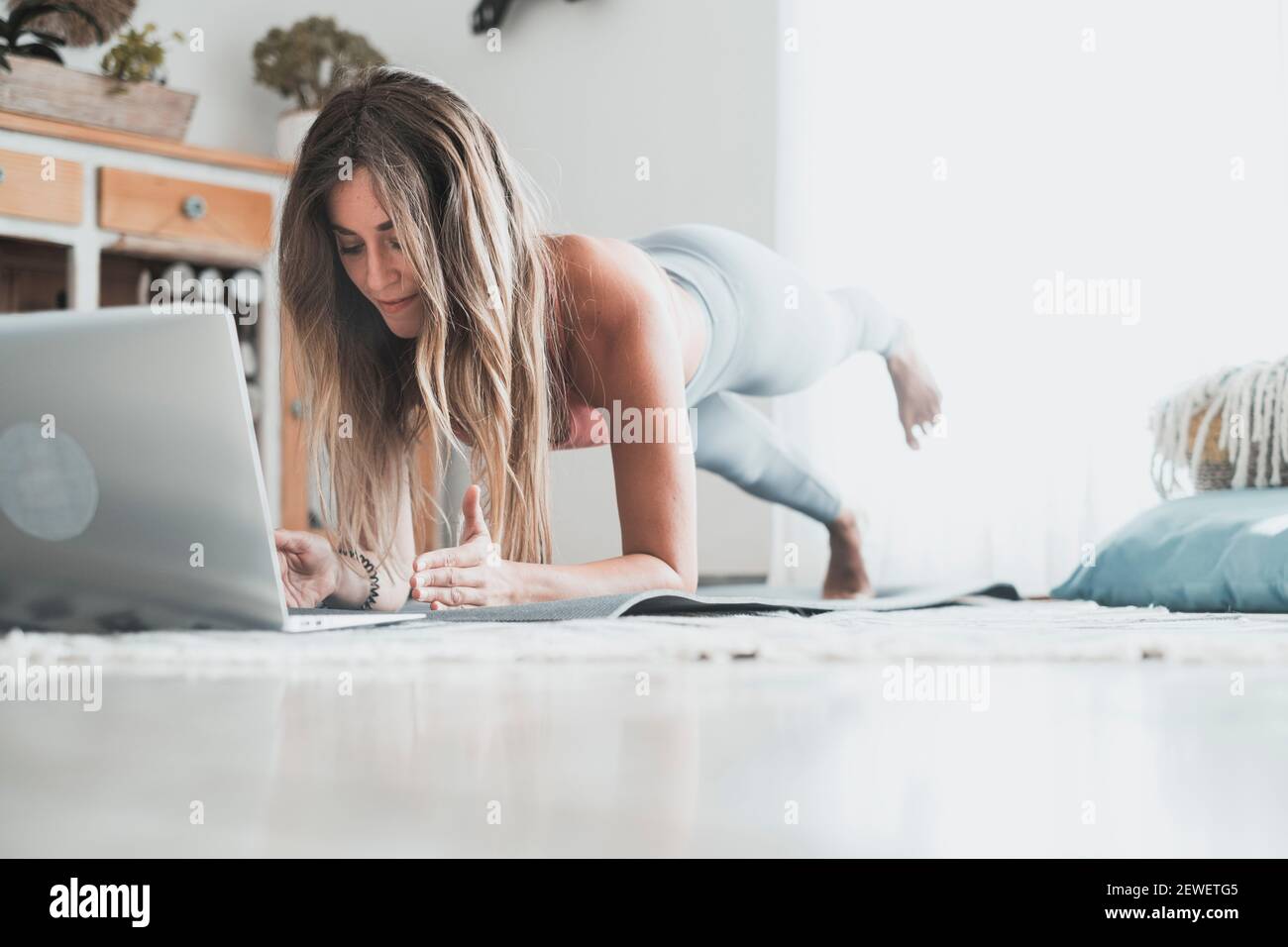 Jeune femme s'exerçant à la maison faisant des push-up et regardant sur son ordinateur portable personnel pour apprendre ou enseigner l'entraînement - force de la planche forme du corps workou Banque D'Images