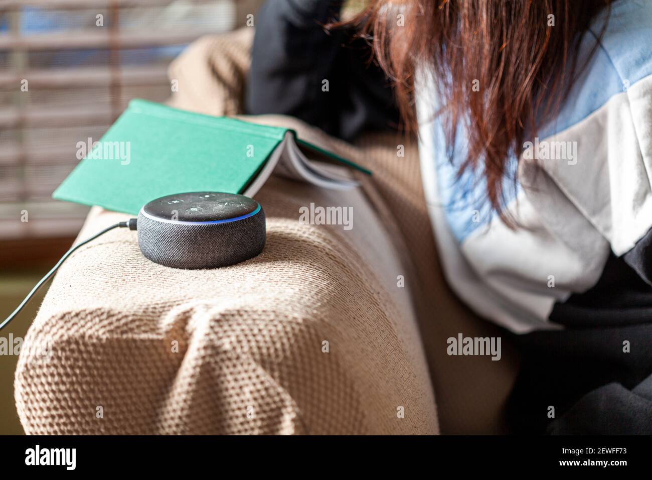 Clarksburg, MD, USA 03-01-2021: Une femme caucasienne assise sur un fauteuil avec des vêtements décontractés dans sa maison pose une question à Amazon Echo Dot, voi Banque D'Images