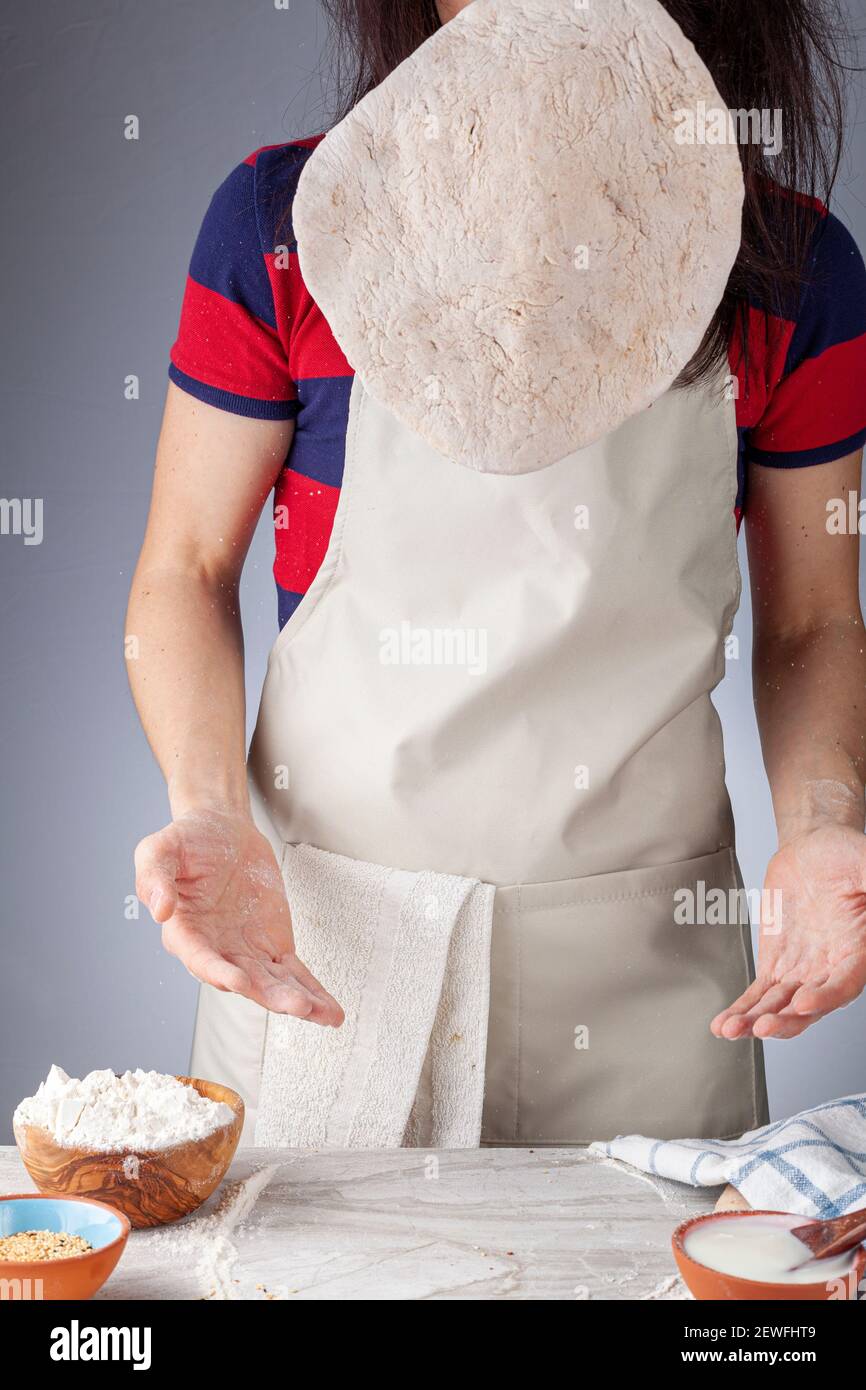 Préparation de base de pain plat, de pide ou de pizza dans la cuisine. La baker femelle lance la base à genoux et aplatie dans l'air f Banque D'Images