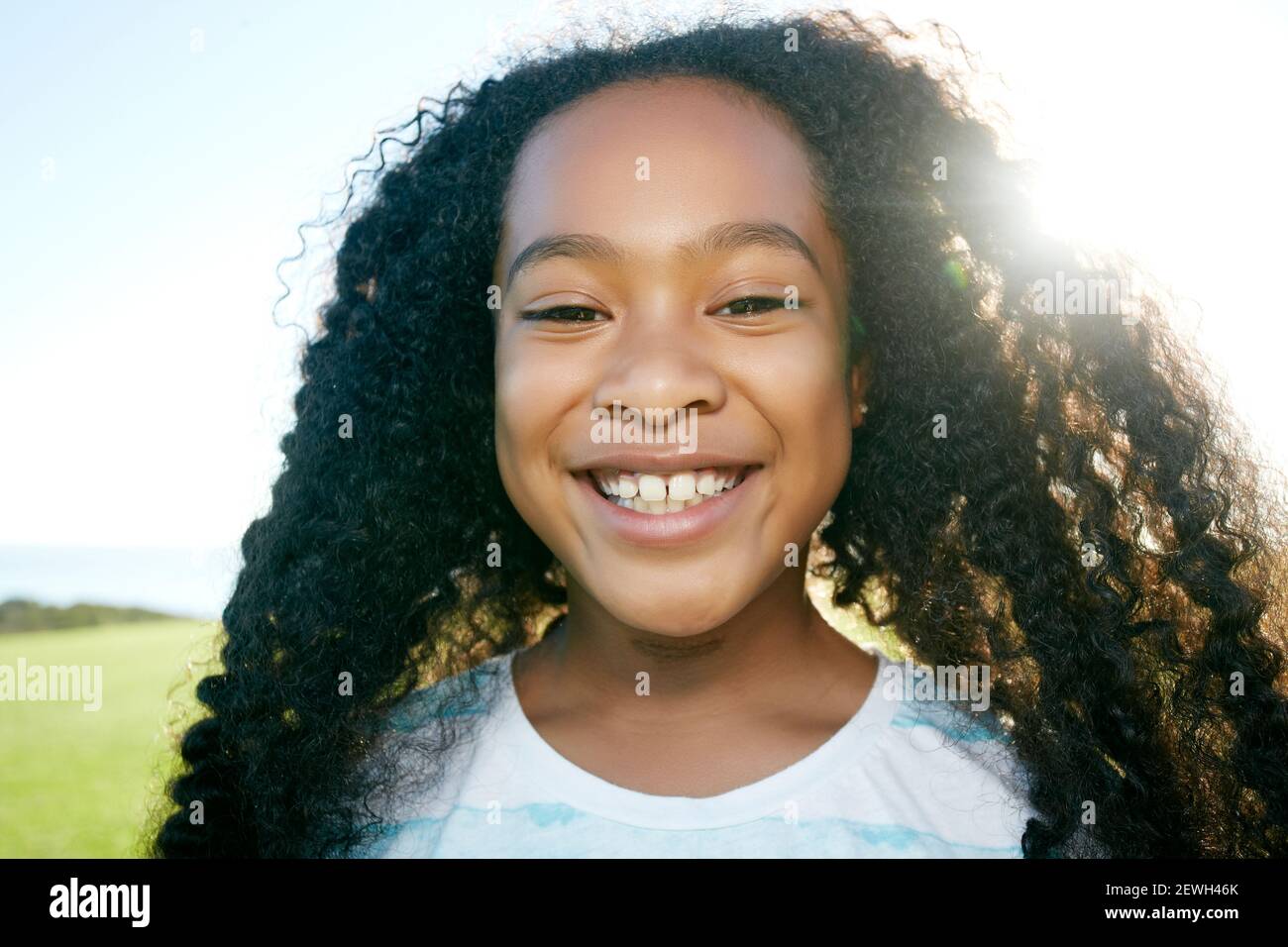 Jeune fille de race mixte avec de longs cheveux bouclés noirs, souriant Banque D'Images