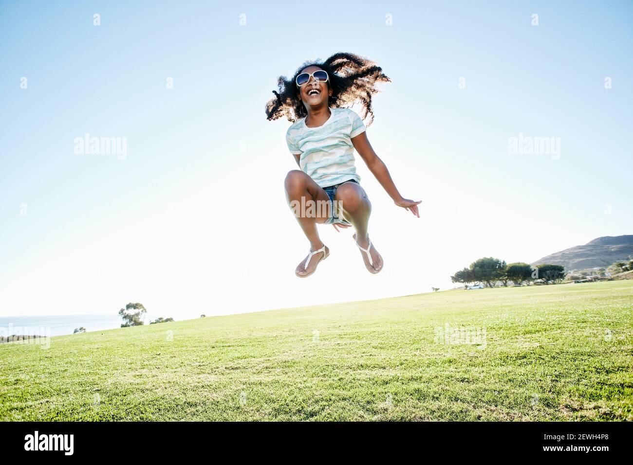 Jeune fille de race mixte avec de longs cheveux bouclés sautant l'air Banque D'Images