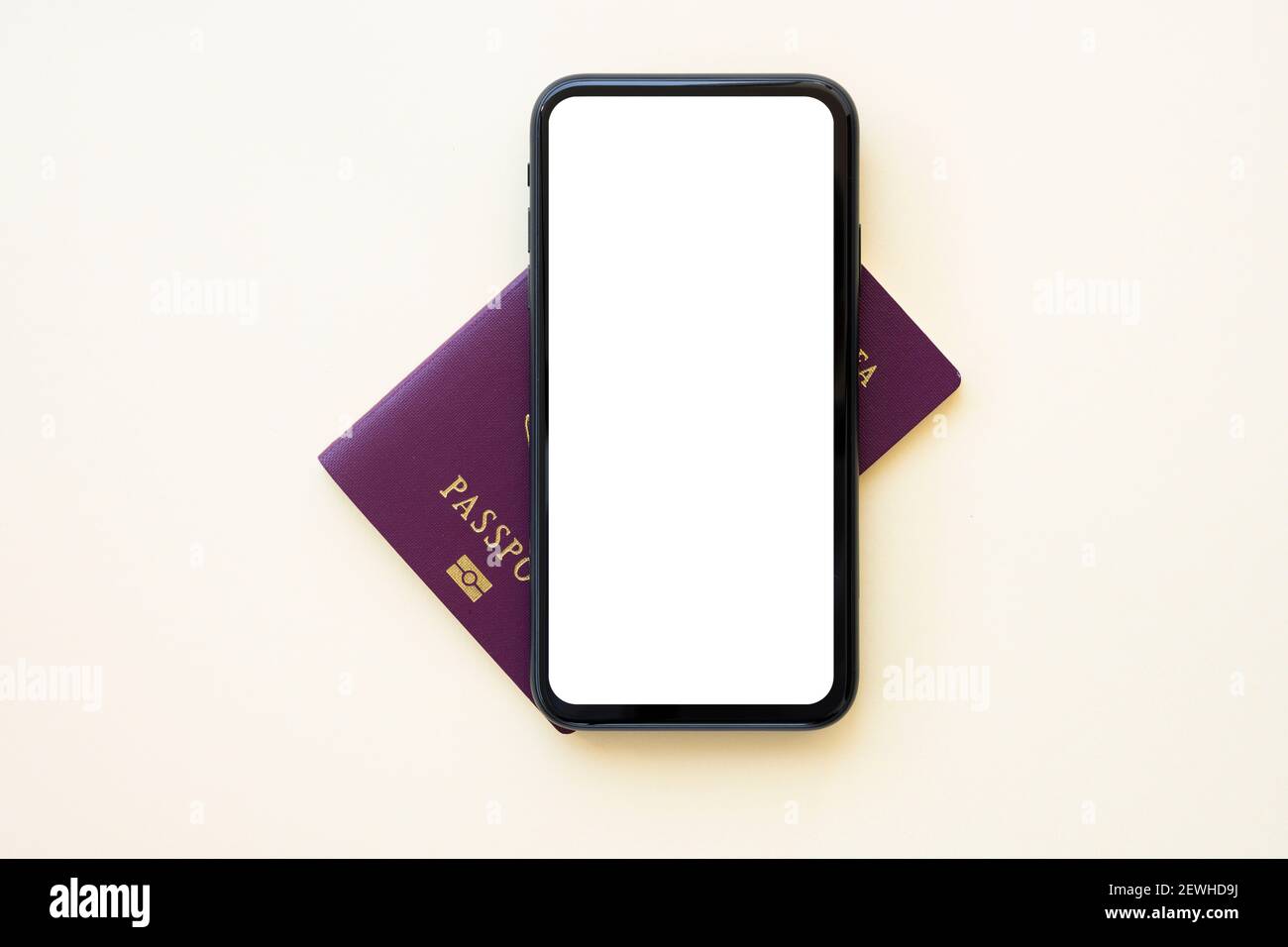 Un plan de travail avec espace de copie, un passeport et un smartphone avec écran blanc sont disposés sur un arrière-plan de couleur crème. Banque D'Images