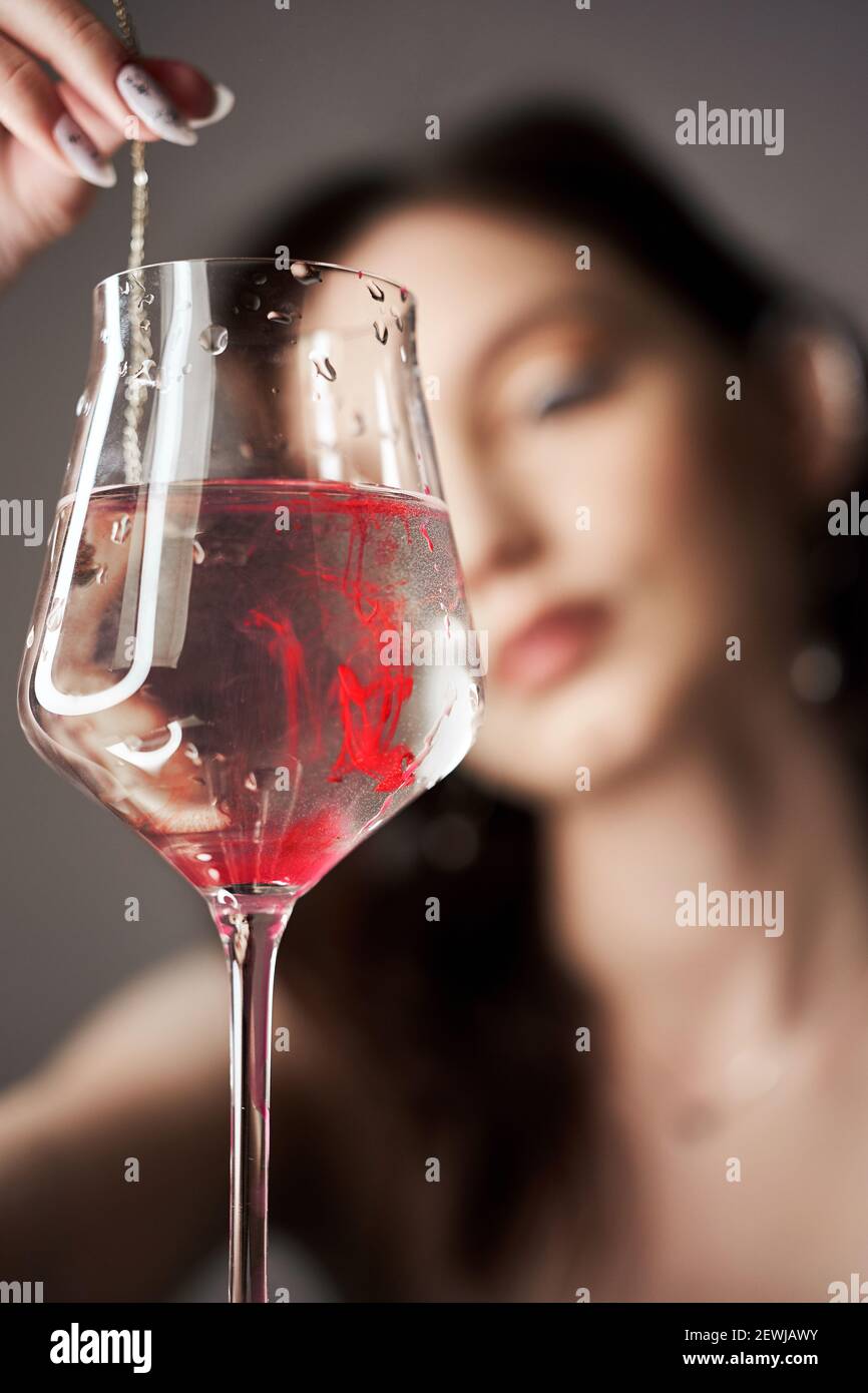 Gouttes de peinture rouge dans un verre d'eau, une femme regarde le verre. Banque D'Images