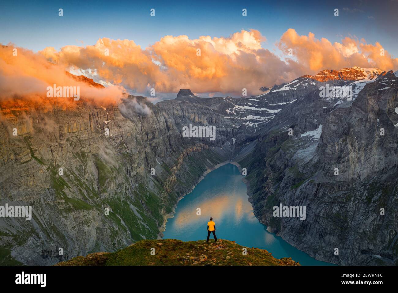 Homme debout sur des rochers regardant les nuages au coucher du soleil sur le lac Limmernsee, vue aérienne, canton de Glaris, Suisse, Europe Banque D'Images