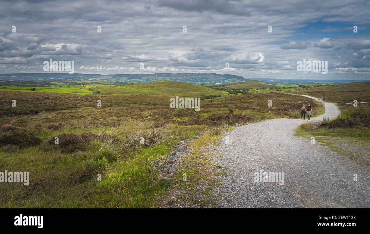 Personnes marchant sur le sentier entre les collines vertes et les champs avec orageux, ciel spectaculaire en arrière-plan, Cuilcagh Mountain Park, Irlande du Nord Banque D'Images