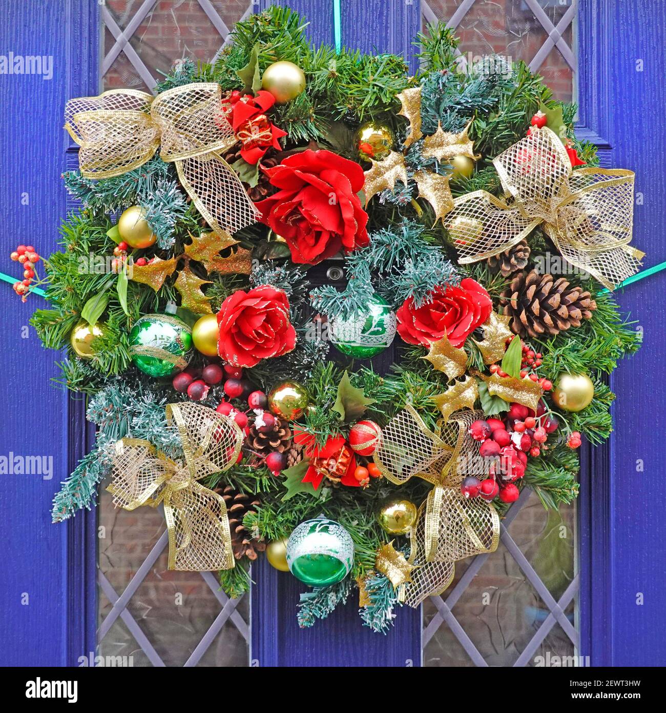 Gros plan de la porte avant de la maison bleue et de la couronne de Noël Avec des décorations de Noël y compris des boules de sapin cône ruban et Fleurs artificielles Angleterre Royaume-Uni Banque D'Images
