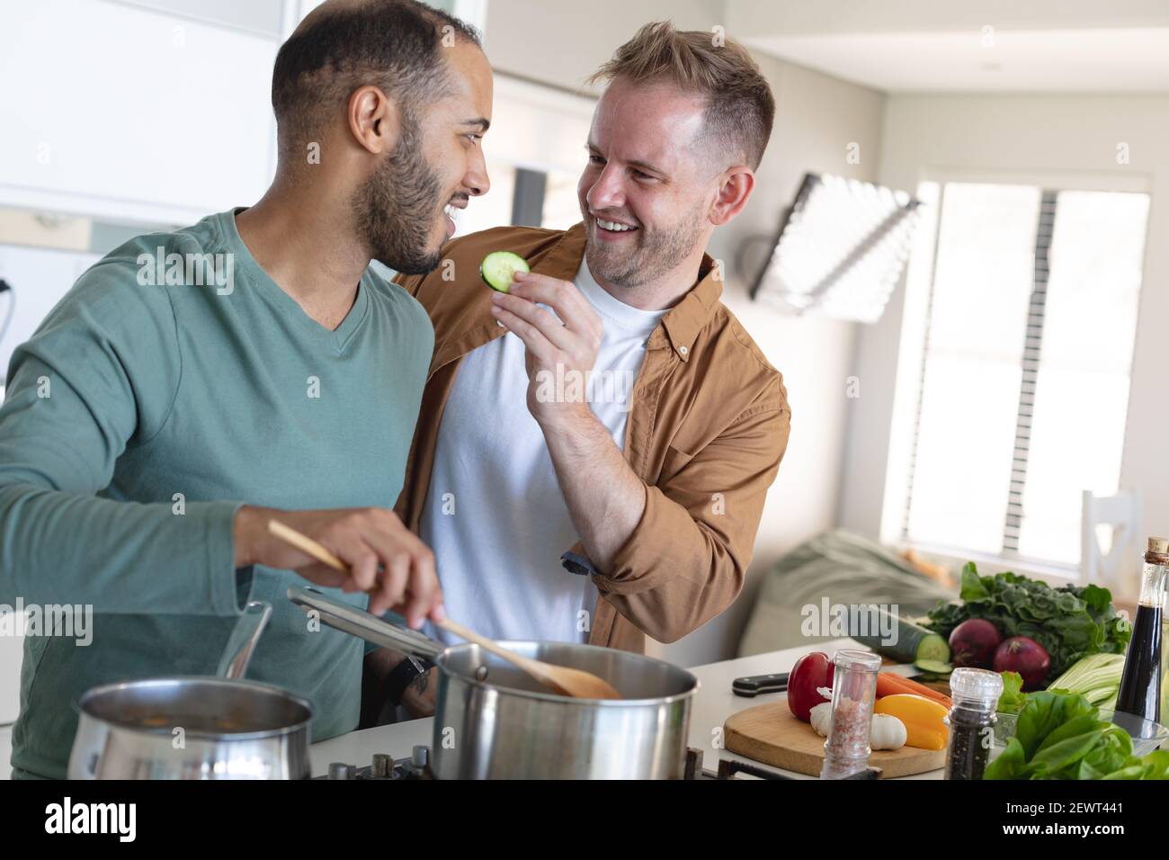 Couple multiethnique gay masculin souriant et préparant la nourriture ensemble à la maison Banque D'Images