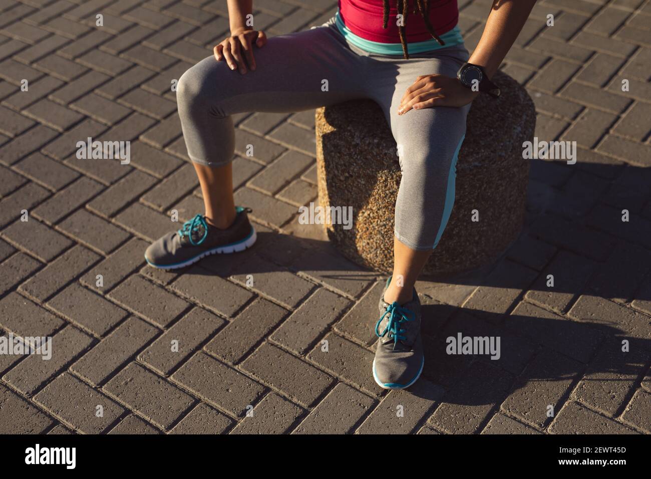 Mi-section de femme afro-américaine prenant une pause dans l'exercice sur une promenade au bord de la mer, assis Banque D'Images