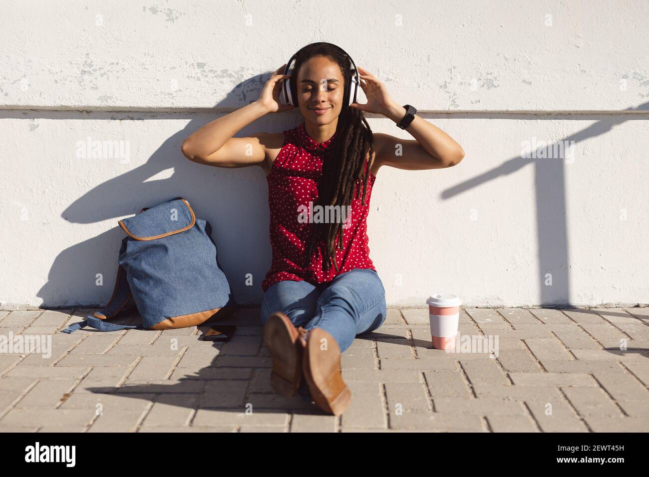 Bonne femme afro-américaine souriante avec les yeux fermés, assise sur le trottoir et à l'écoute de musique Banque D'Images