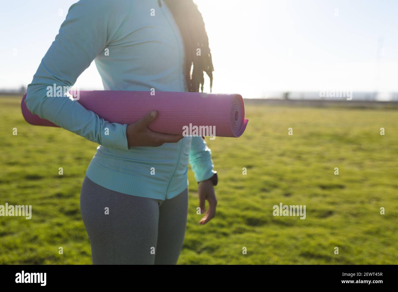 Section moyenne d'une femme afro-américaine s'exerçant dans un parc transportant un tapis de yoga Banque D'Images