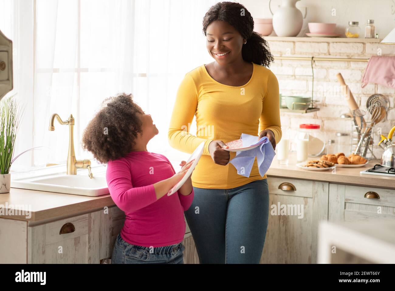 Petite fille noire Wiping plats avec maman dans la cuisine Banque D'Images