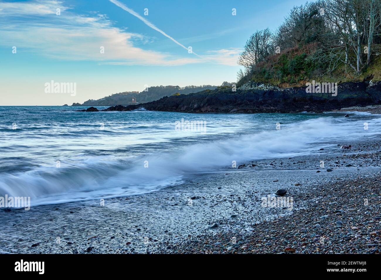 Image d'une plage de stoney en fin de soirée avec la Tour de Jersey Archirondel au fond lointain et des vagues de rupture avec ciel bleu avec un peu de nuage. Jersey, Cha Banque D'Images