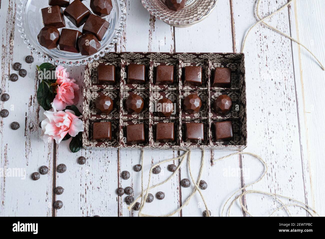 Boîte brune de bonbons au chocolat, à côté des fleurs, des noix de callettes au chocolat et des cordes à ficelle. Banque D'Images