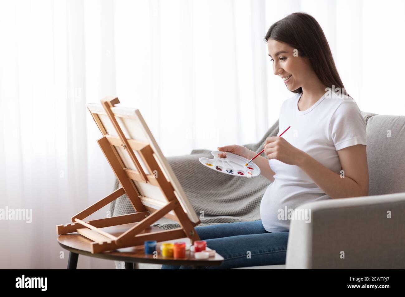 Femme enceinte positive peinture sur Easel, séance d'art thérapeutique à domicile Banque D'Images