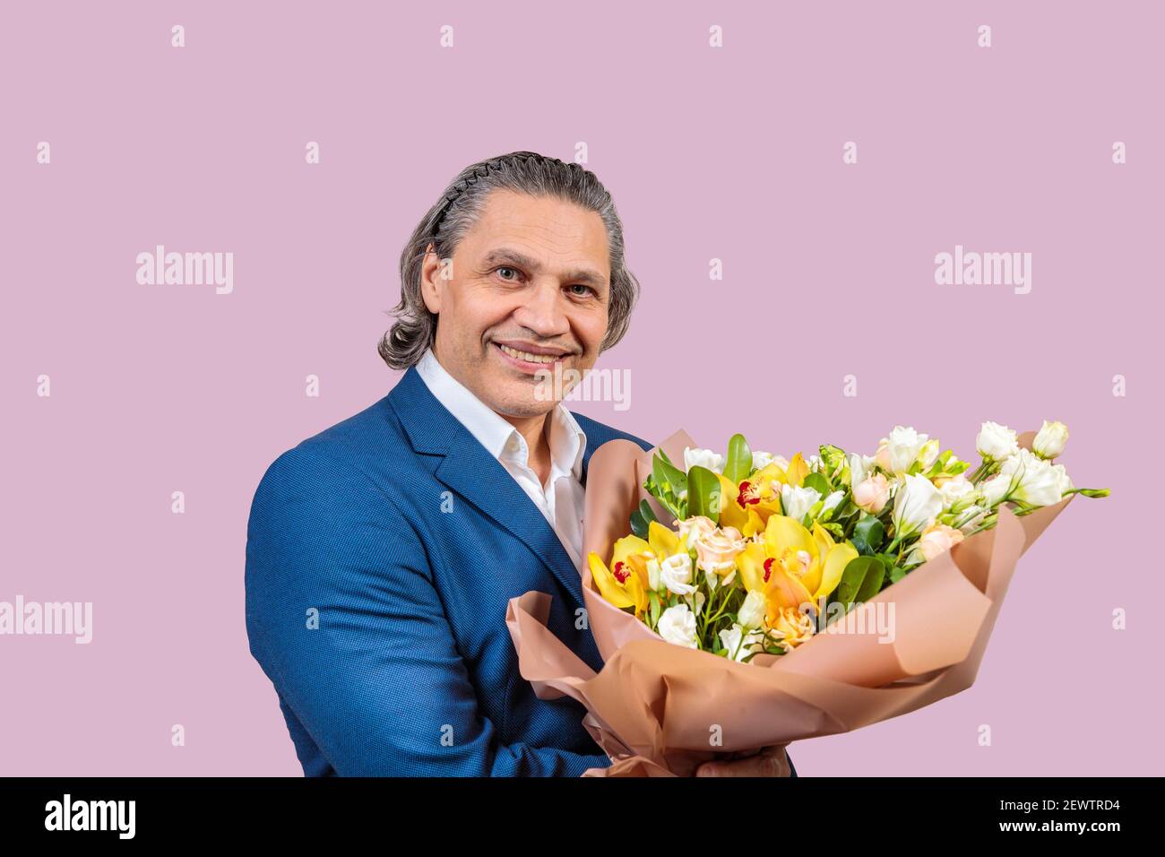 Homme souriant de 50 ans dans une veste bleue avec un bouquet de fleurs sur un fond uniforme. Cheveux longs gris Banque D'Images