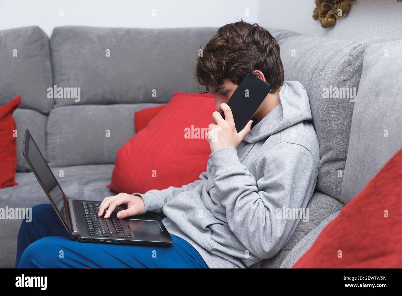 un jeune homme parle au téléphone et travaille sur l'ordinateur portable. soyez à la maison en période de pandémie Banque D'Images