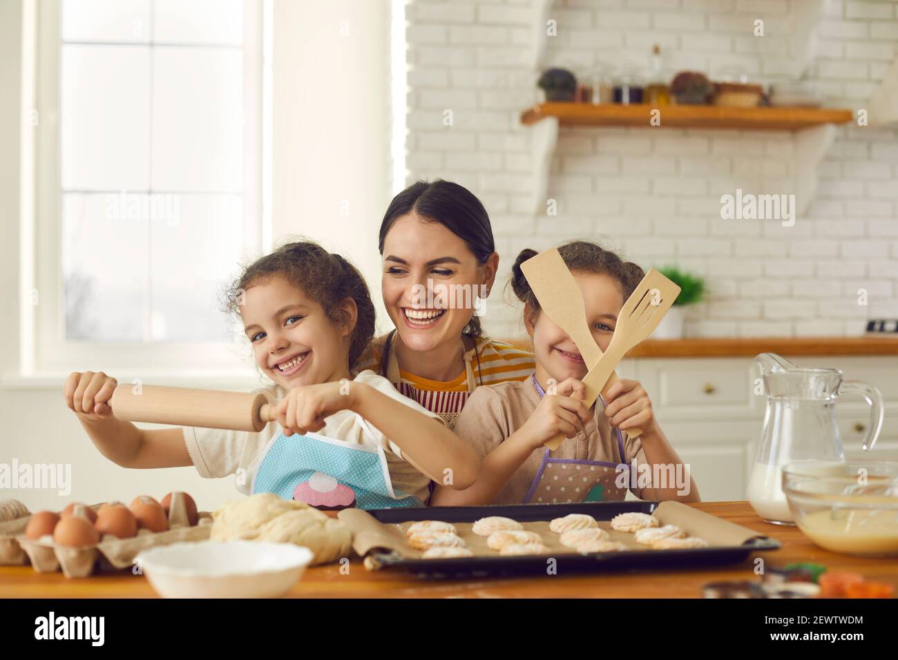 Une jeune mère heureuse et ses filles utilisant un rouleau et spatules en bois pendant la cuisson Banque D'Images