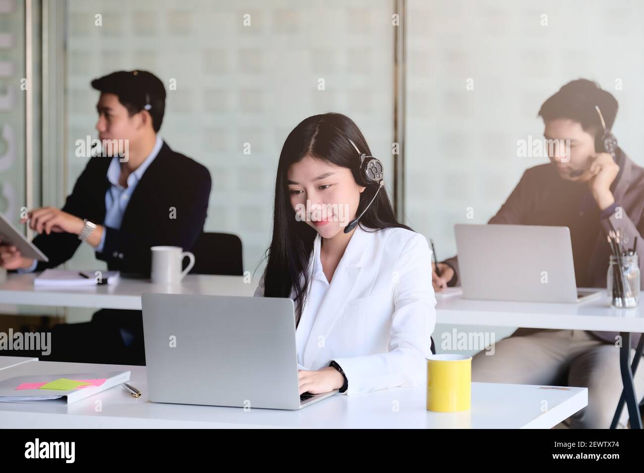 Jeune femme asiatique travaillant dans un centre d'appels, entourée de collègues. Banque D'Images