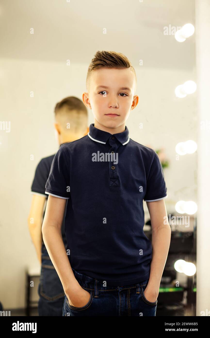 garçon de 10 ans dans un coiffeur après une coupe de cheveux à la mode  devant un miroir.Un petit enfant dans un salon de beauté regarde la caméra  poser Photo Stock 