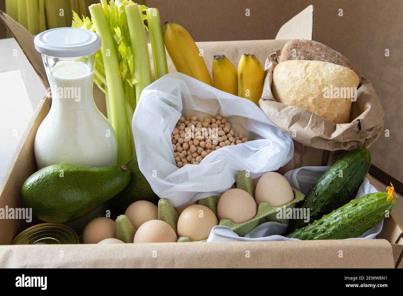 Boîte à nourriture sur la table. Il contient du lait, des bananes, des pois chiches, des concombres, du céleri, œufs, pain, avocat. Concept de livraison de nourriture, zéro déchet, écologique, Banque D'Images