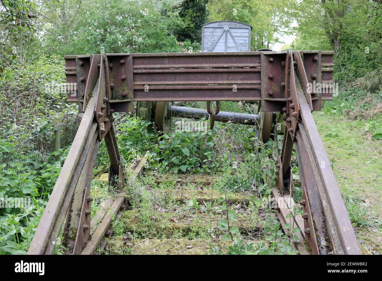 Heritage ligne de chemin de fer magasin extérieur avec des tampons, roues de bogie avec et sans chariot de marchandises sur la courte section de voie avec de grands arbres. Banque D'Images