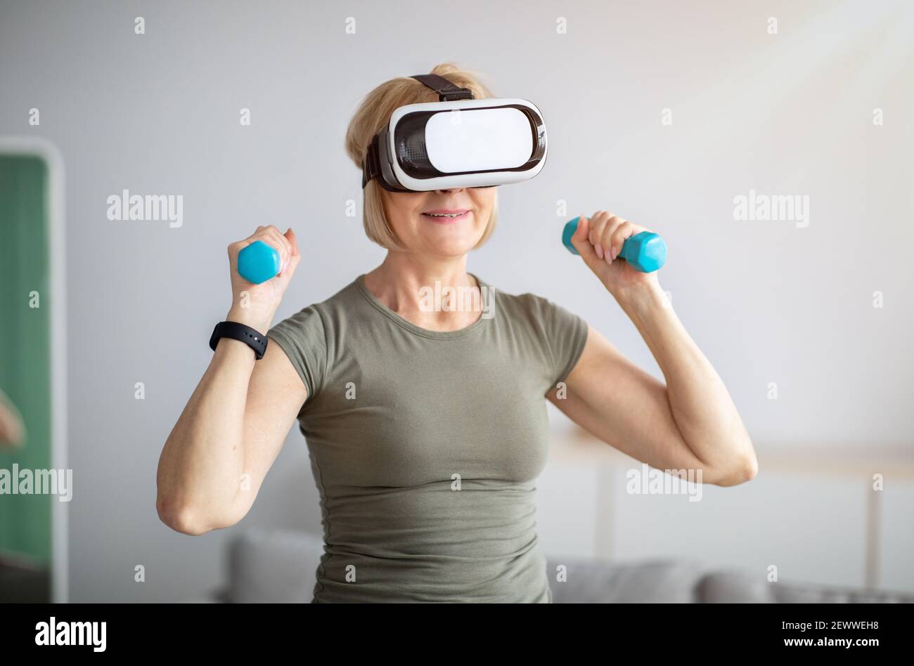Une femme mûre s'entraîne avec des haltères, portant un casque de réalité virtuelle, ayant un entraînement domestique. Fitness futuriste Banque D'Images