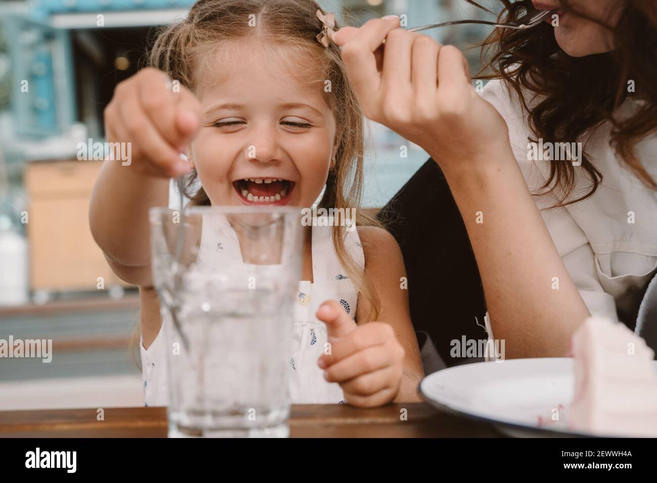 Petite fille avec maman jouant avec des glaçons dans un café confortable. Banque D'Images