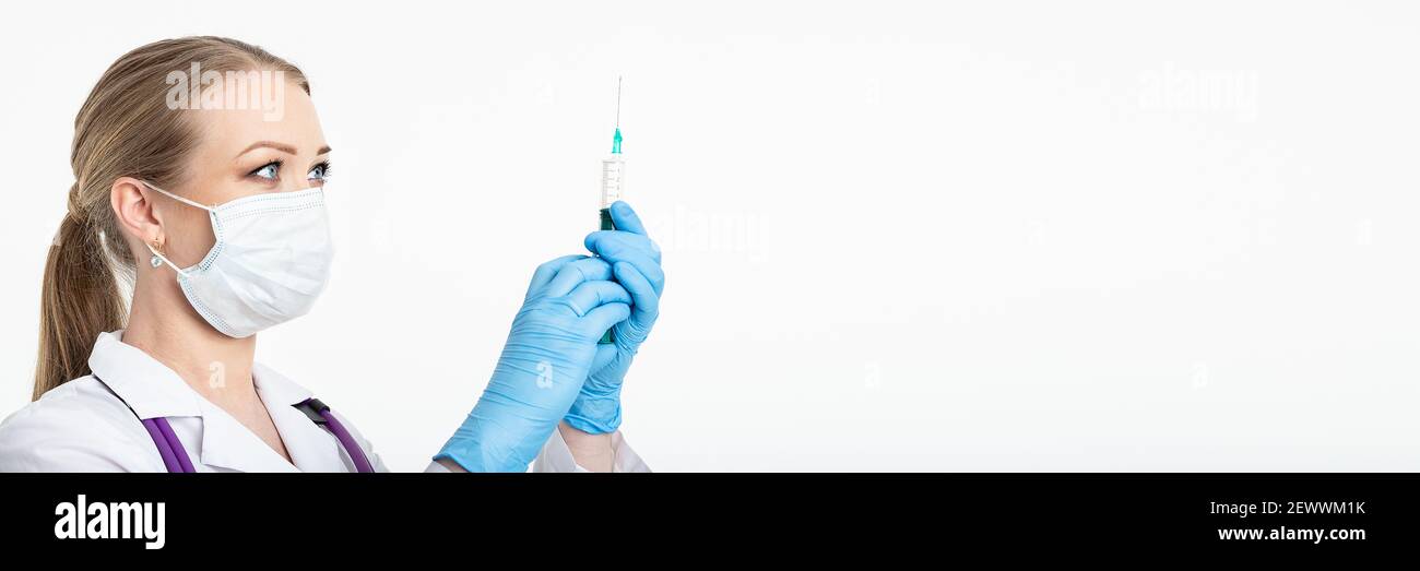 Une jeune infirmière dans un masque compose le vaccin dans une seringue tout en étant assise dans un hôpital à côté d'un patient. Patiente en attente de l'injection de la grippe Banque D'Images