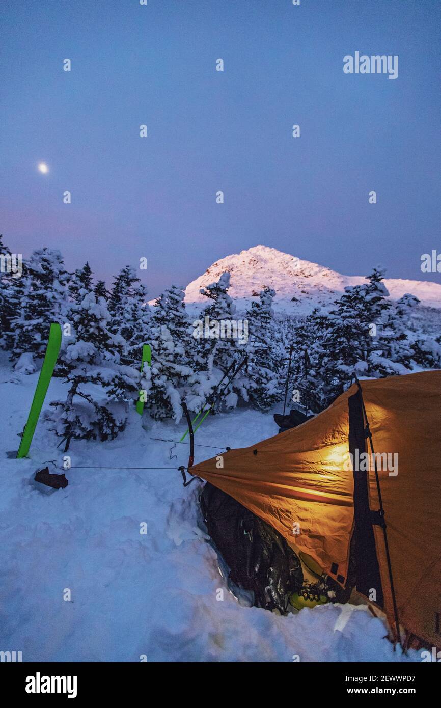 Camping d'hiver avec tente dans les montagnes enneigées au crépuscule, New Hampshire Banque D'Images