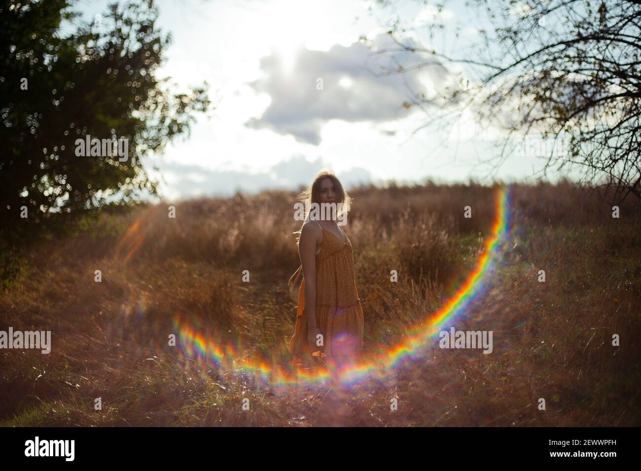 Une jeune femme en robe se tient dans un foin le champ avec une lumière d'objectif met en évidence son cadre Banque D'Images