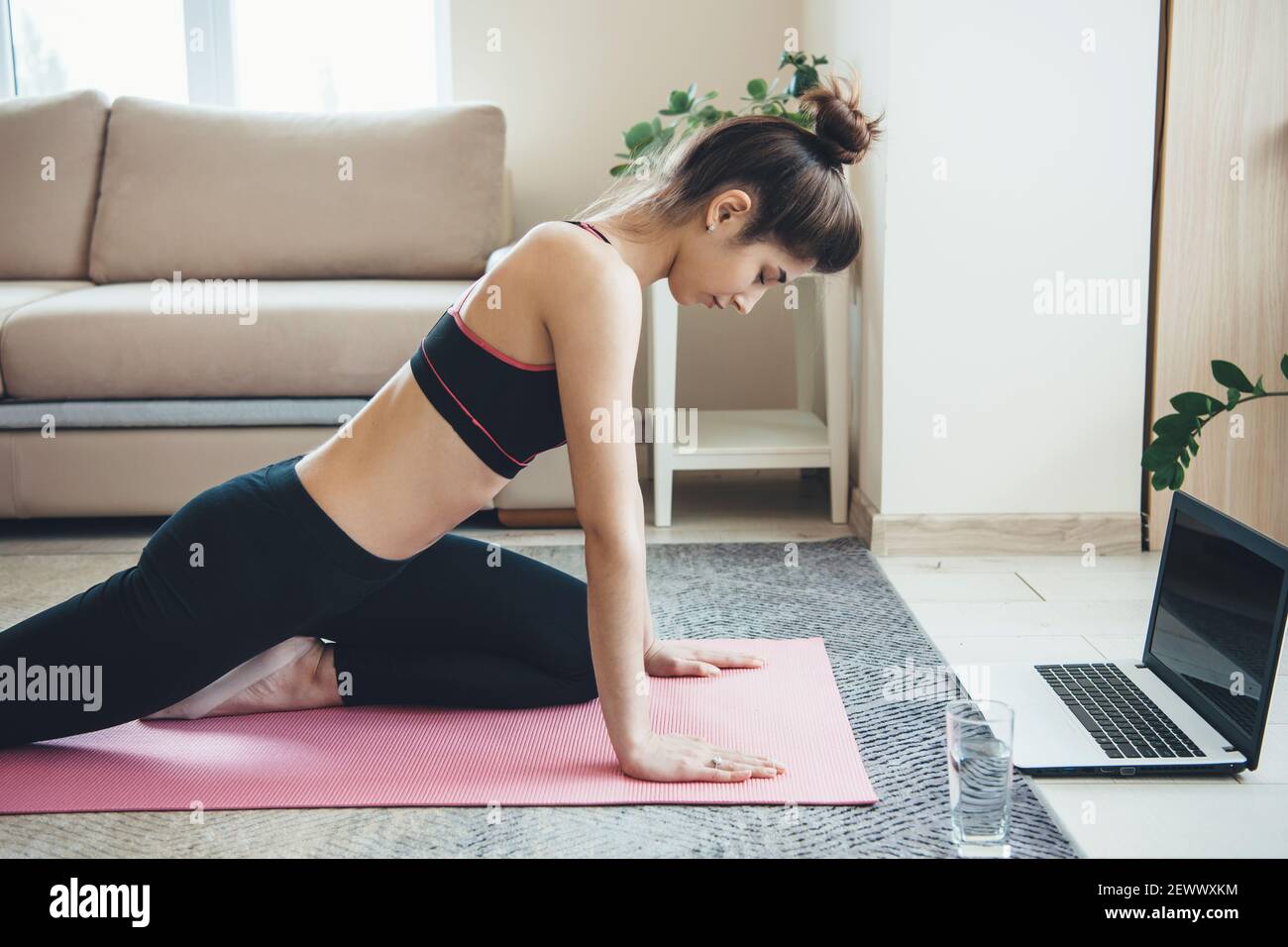 La femme caucasienne portant des vêtements de sport fait des exercices de remise en forme sur le sol avec un ordinateur portable et un verre avec de l'eau Banque D'Images