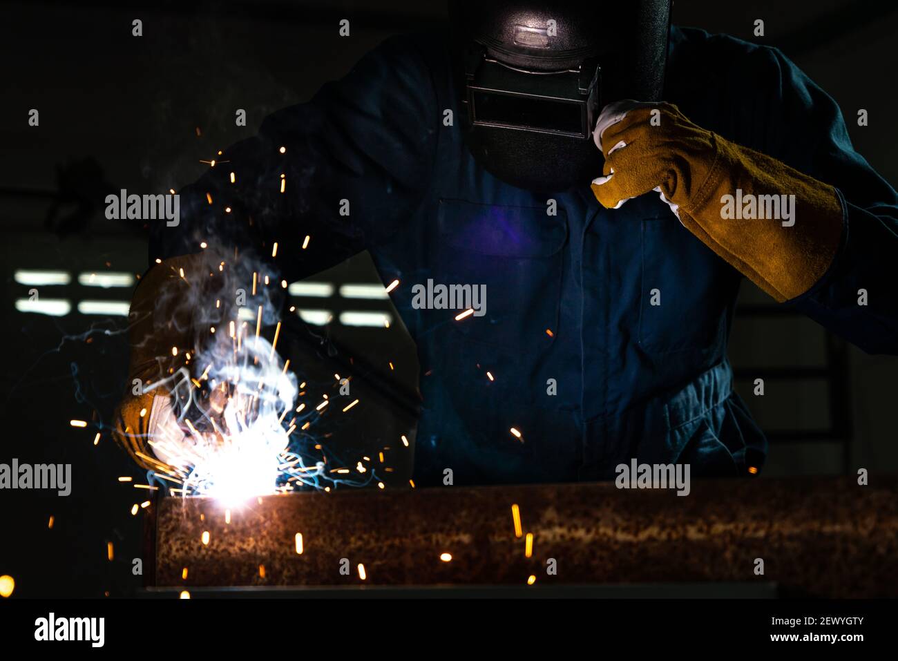 Soudeur de métal travaillant avec une machine à souder à l'arc pour souder l'acier en usine tout en portant un équipement de sécurité. Fabrication et construction de métaux Banque D'Images