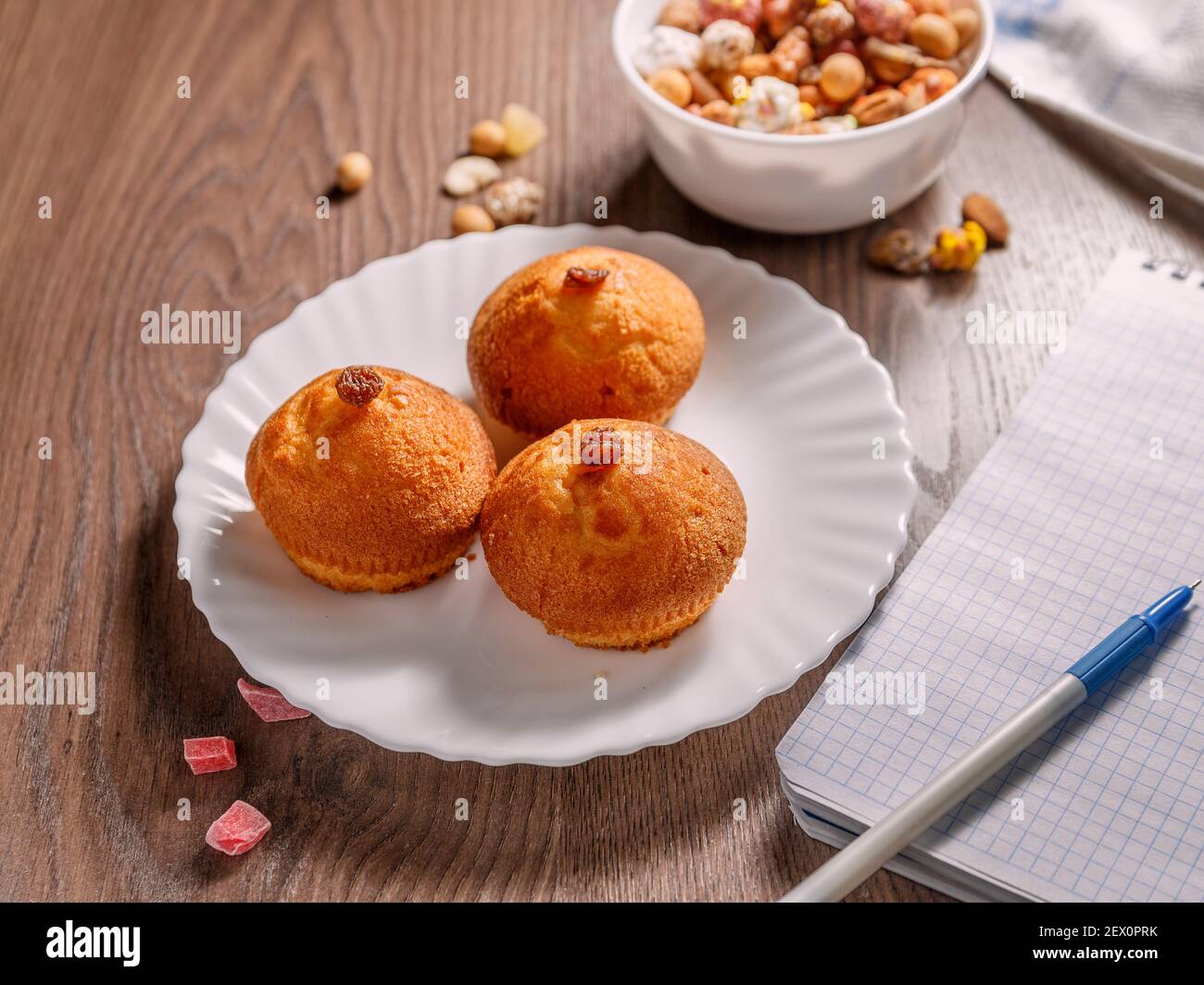 Délicieux petits gâteaux dans une assiette blanche à côté d'une assiette de noix et carnet avec stylo sur une surface brune. Mise au point sélective Banque D'Images