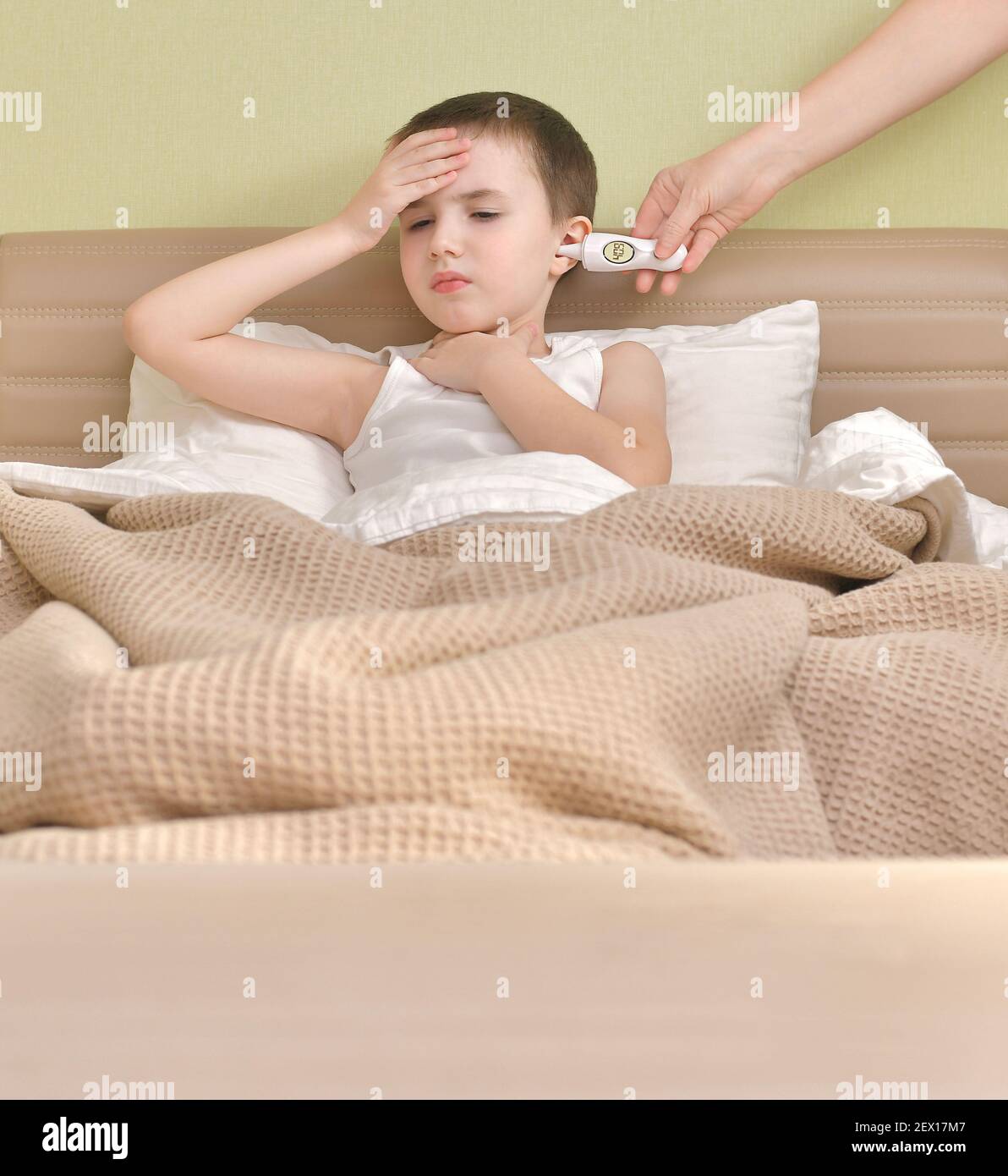 Un enfant malade est au lit. Mesure de la température élevée à l'aide d'un thermomètre auriculaire. Banque D'Images