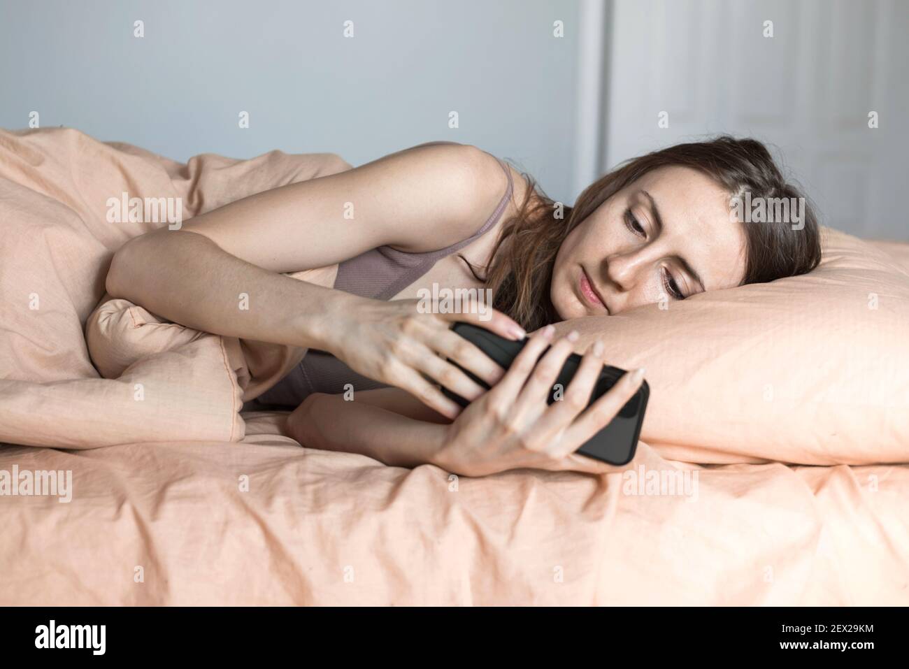 jeune femme regardant l'écran du smartphone dans le lit Banque D'Images