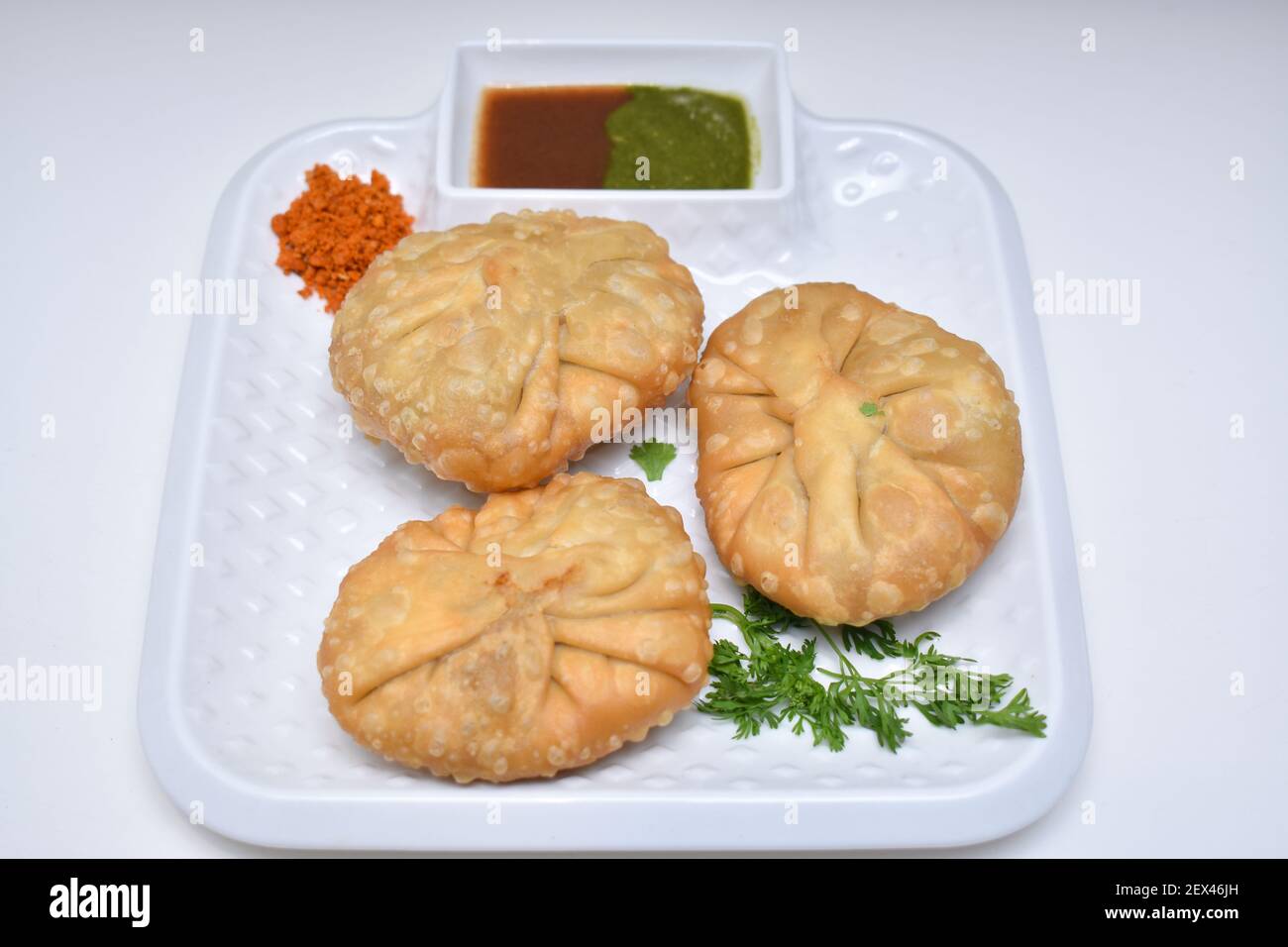 Kachori avec chutney à l'ail sec garni de feuilles de coriandre kachori est un en-cas épicé de l'Inde également orthographié comme kachauri et kachodi. Fond blanc Banque D'Images