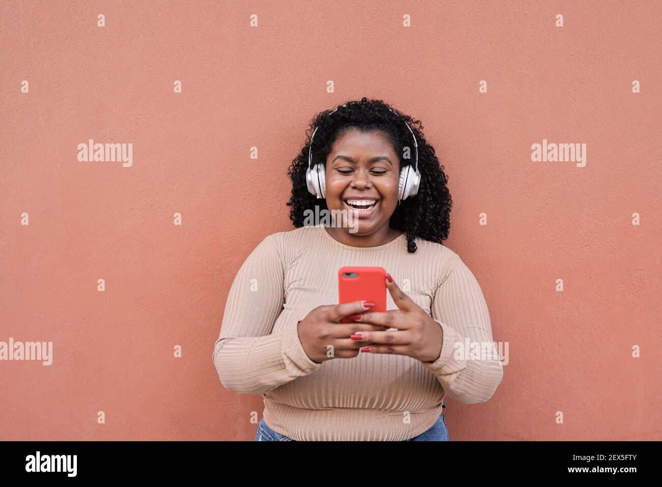 Une jeune fille africaine aux courbes qui écoute de la musique d'une liste de lecture tout en regardant Sur téléphone mobile - jeune fille millénaire s'amusant avec la technologie Tendances - Focus sur fa Banque D'Images