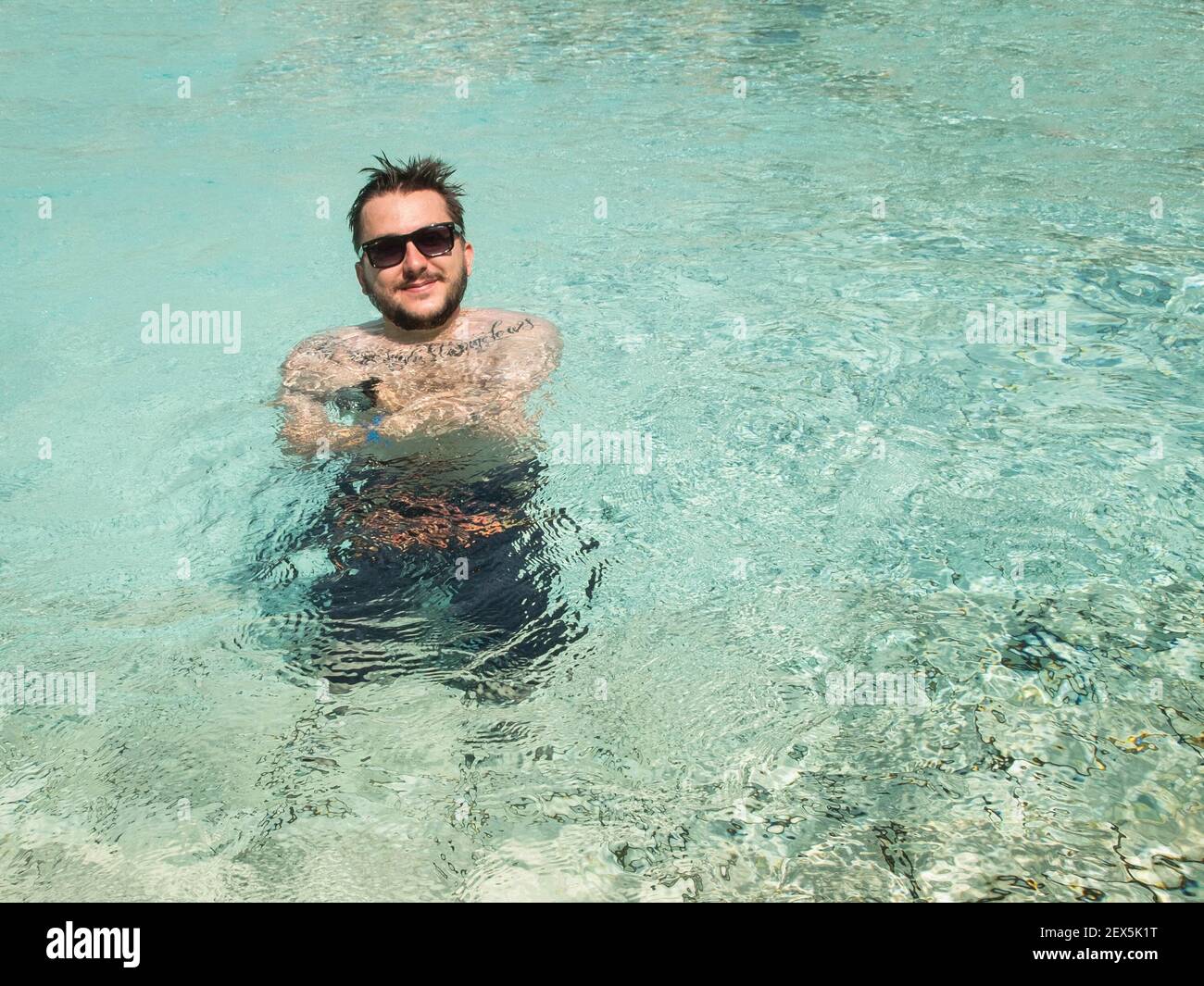 Un jeune homme adulte porte des lunettes de soleil à la piscine Banque D'Images