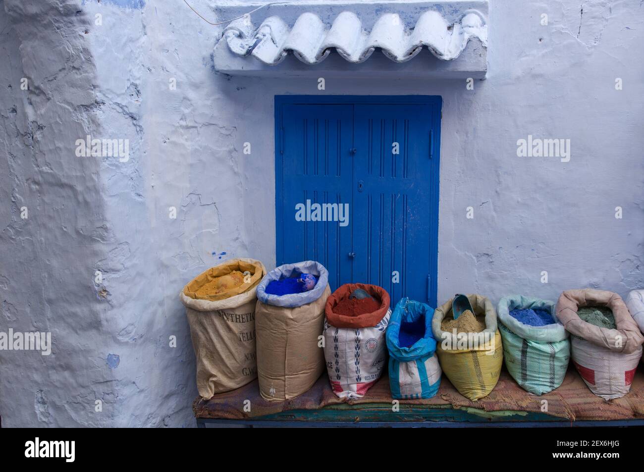Maroc, Chefchaouen, architecture de la ville bleue des bâtiments blanchis à la chaux blanc et indigo, avec sacs de pigments de peinture colorés en vente Banque D'Images