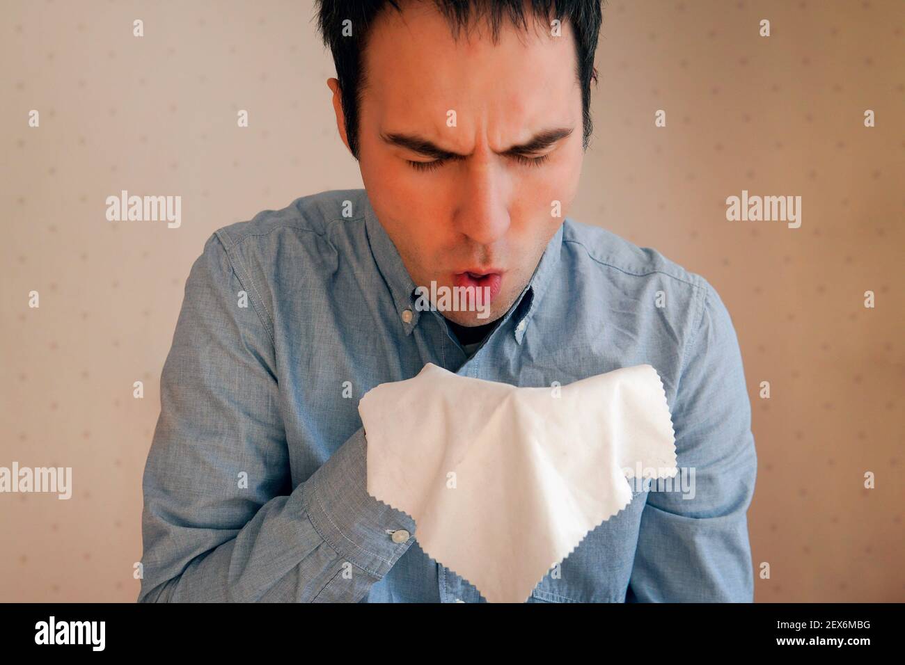 Guy tousse. Éternuez dans un chiffon. Un jeune caucasien attrayant tousse intensivement et couvre sa bouche avec une serviette. Rhume, grippe, mal de gorge, respira aiguë Banque D'Images