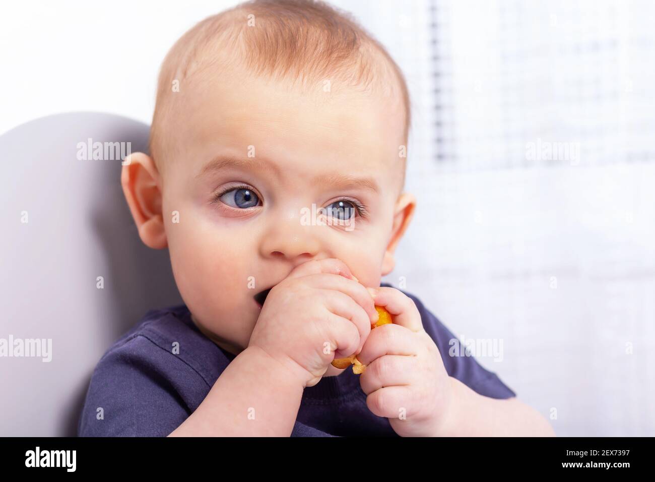 Mignon petit garçon caucasien est assis dans une chaise haute et manger de la banane avec les mains. Gros plan sur le visage d'enfant sale. Banque D'Images